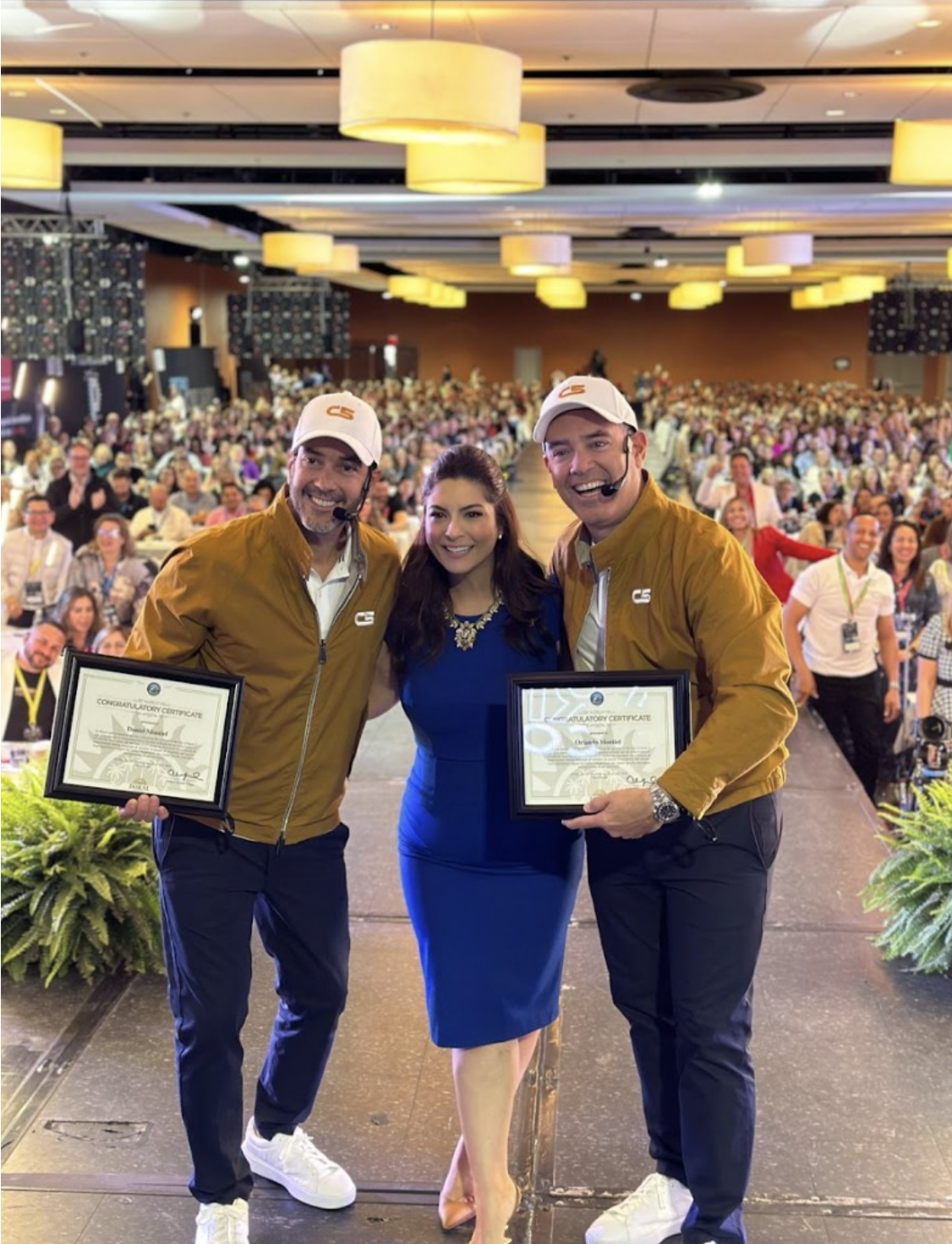 Mayor Christi Fraga entregando el Congratulatory Certificate de la City of Doral a Orlando y Daniel Montiel en escenario, evento Retiro Inmobiliario · abril 2024